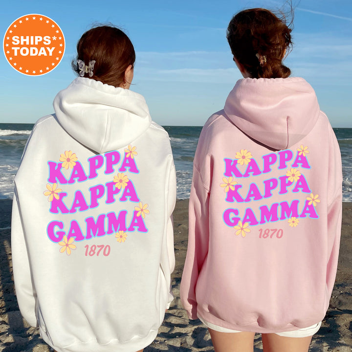 Two women wearing matching white and pink hooded sweatshirts with the Kappa Kappa Gamma logo on the back, standing on a beach with the ocean in the background.