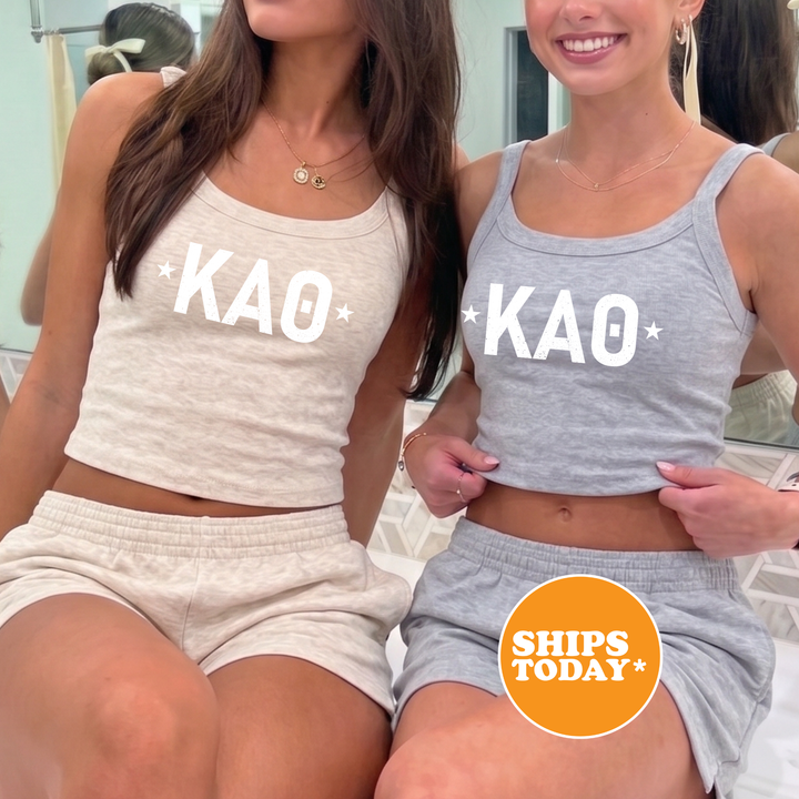 Two women wearing matching gray tank tops with white text and logos, posing together in front of a mirror.