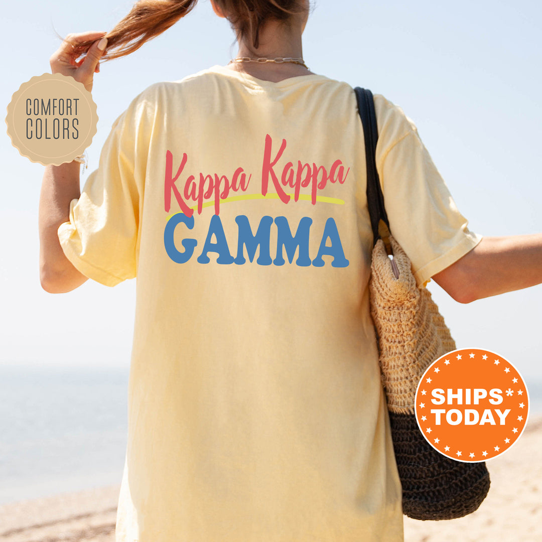 A person wearing a yellow t-shirt with the text " Kappa Kappa Gamma" printed on it, standing on a beach with their hair in a ponytail.