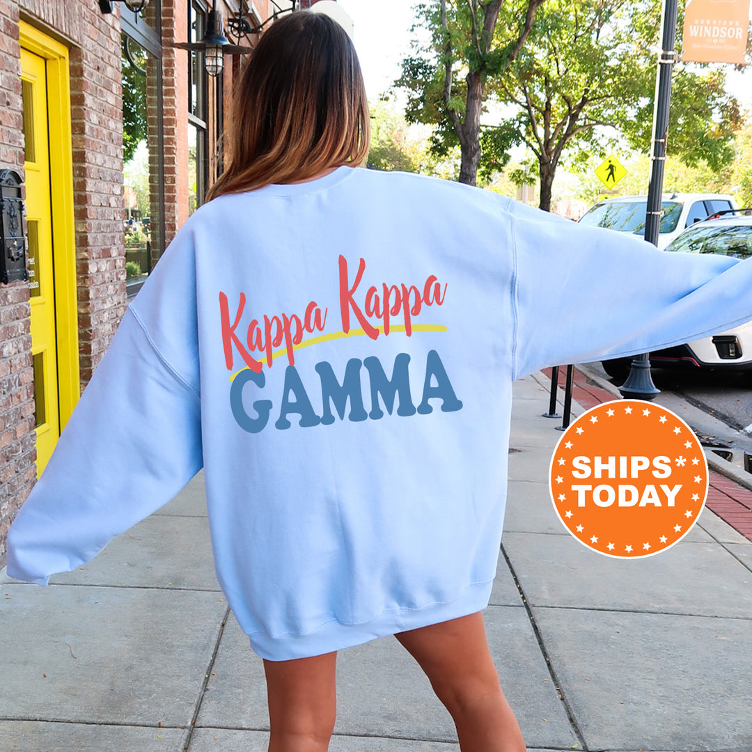 A woman wearing a light blue sweatshirt with the text " Kappa Kappa Gamma" printed on it, standing on a sidewalk.