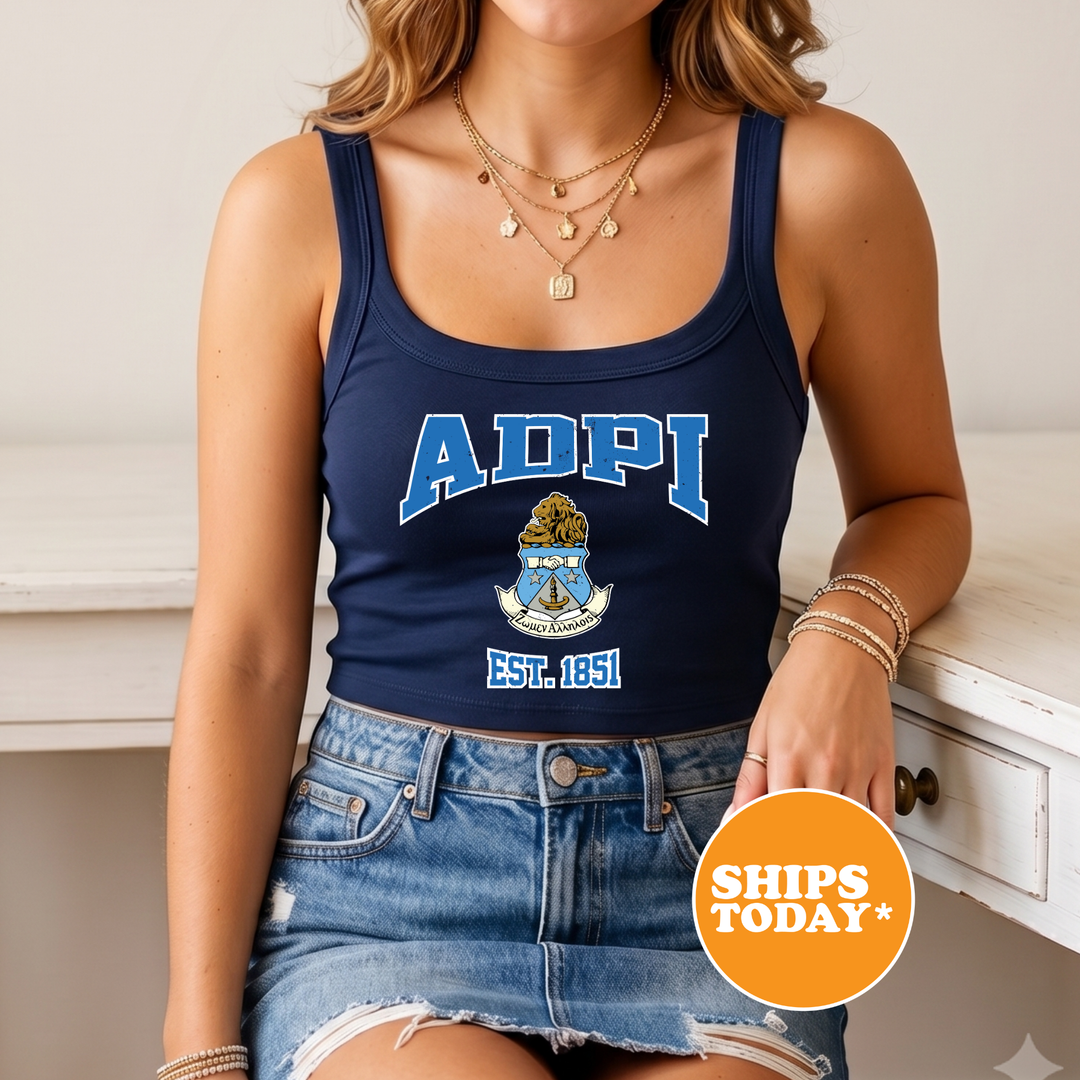 A woman wearing a navy blue tank top with the letters 'ADPI' and a graphic, paired with denim shorts, sits on a white surface.