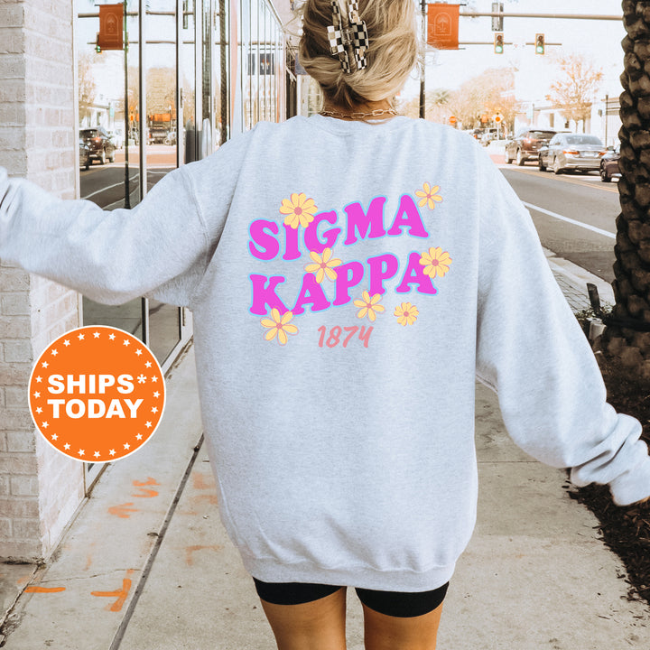 A person wearing a gray sweatshirt with the text "SIGMA KAPPAS 1874" printed on it, standing on a sidewalk with a brick building in the background.