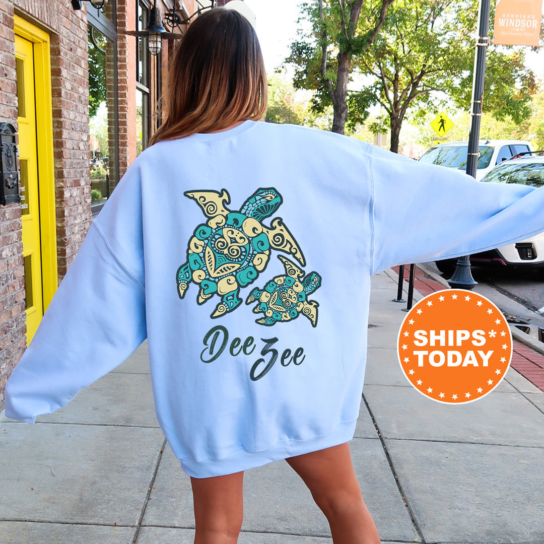 A woman wearing a light blue sweatshirt with a design of a turtle and the name 'Dee' printed on it, standing on a sidewalk.