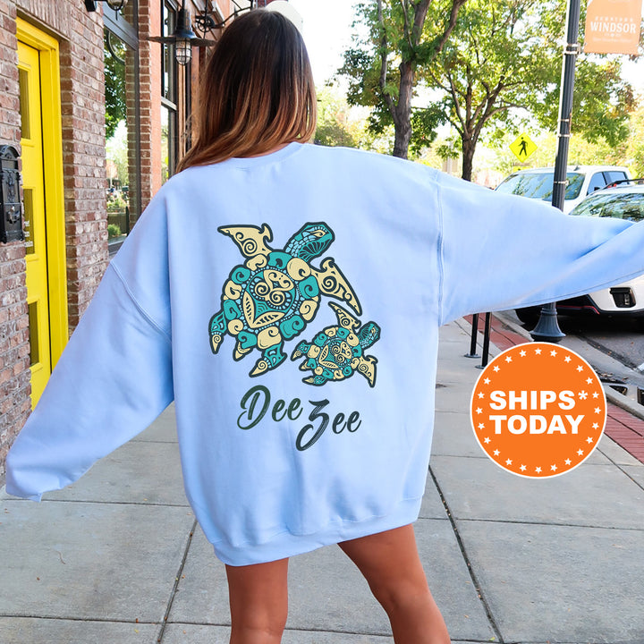 A woman wearing a light blue sweatshirt with a design of a turtle and the name 'Dee' printed on it, standing on a sidewalk.