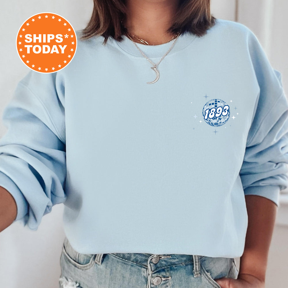 A person wearing a light blue sweatshirt with a blue and white design on the front, and a necklace around their neck.