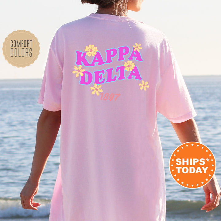 A person wearing a pink t-shirt with the text "KAPPADELTA" printed on it, standing near the ocean.
