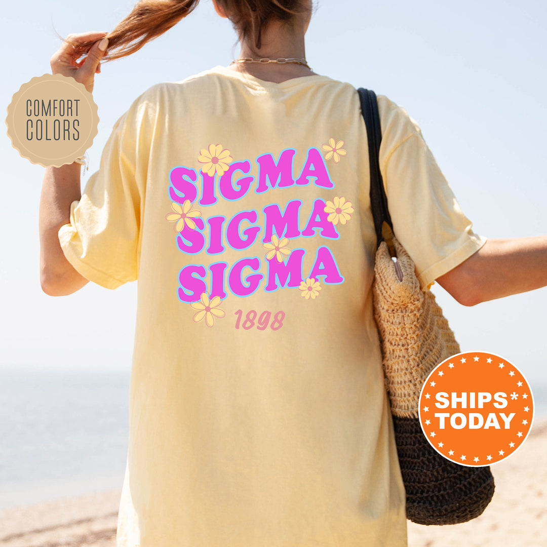 A person wearing a yellow t-shirt with the text "SIGMA SIGMA SIGMA" printed on it, standing on a beach.