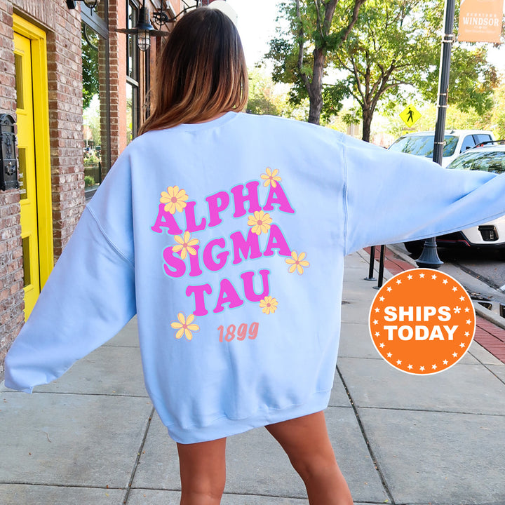 A woman wearing a light blue sweatshirt with pink and yellow text and flowers on the back, standing on a sidewalk.