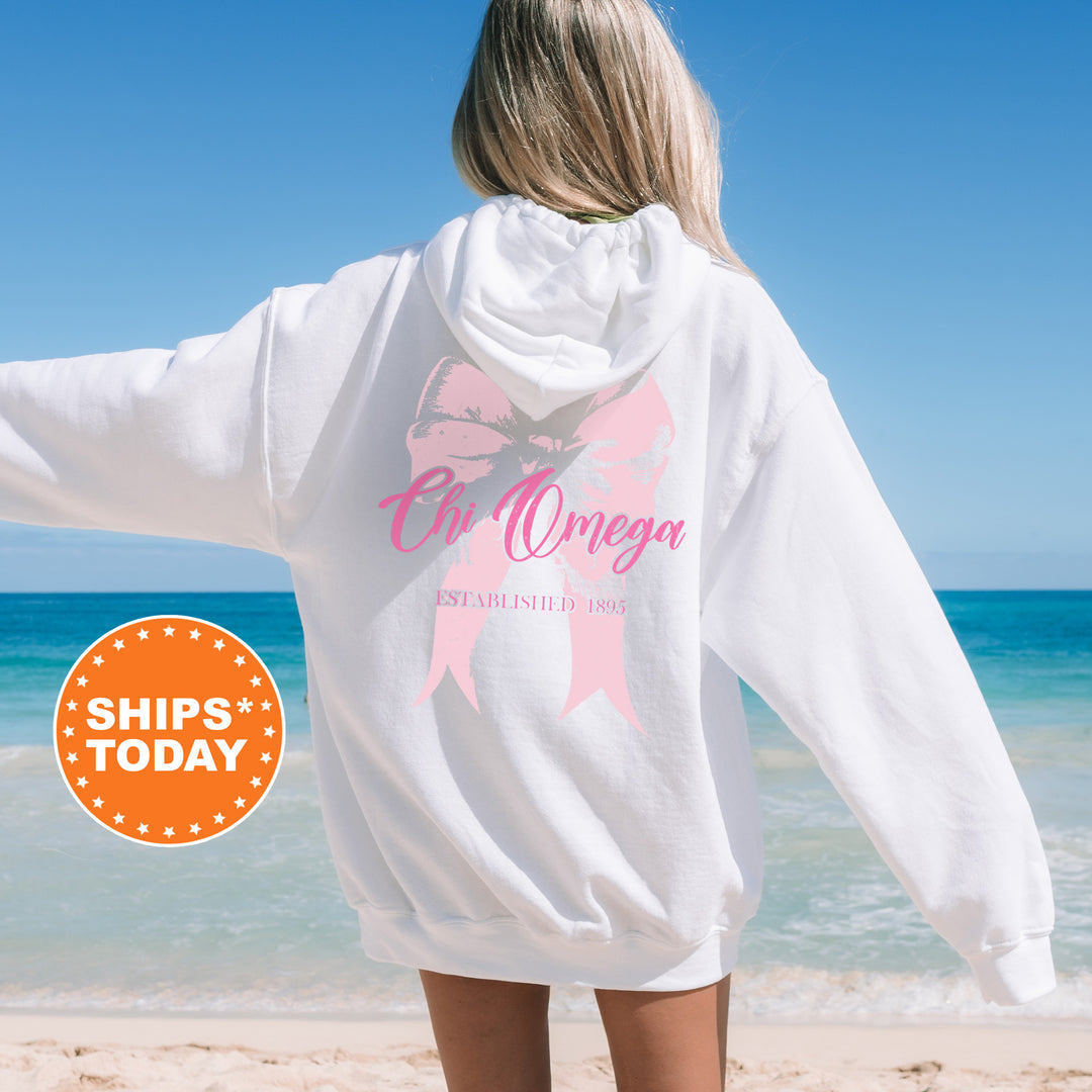 a woman standing on a beach wearing a white sweatshirt with a pink ribbon