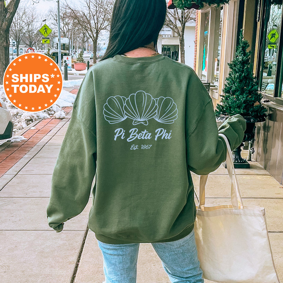 A woman wearing a green sweatshirt with a white graphic of shells and text on the back is walking down a city street.