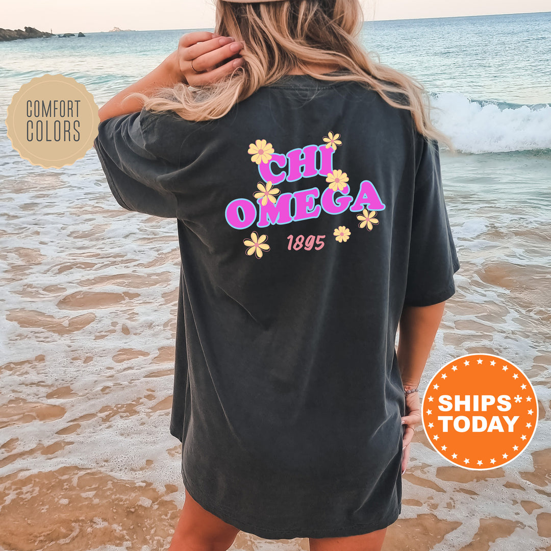 A woman wearing a black t-shirt with the text "CHI OMEGA 1895" printed on it, standing on a beach with the ocean in the background.