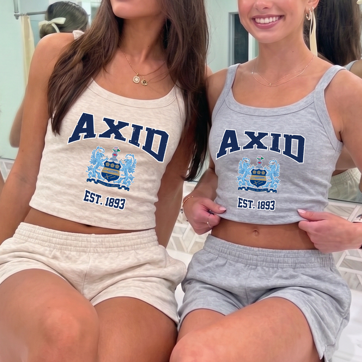 Two women wearing matching crop tops with the word "AXID" printed on them, posing together in front of a mirror.