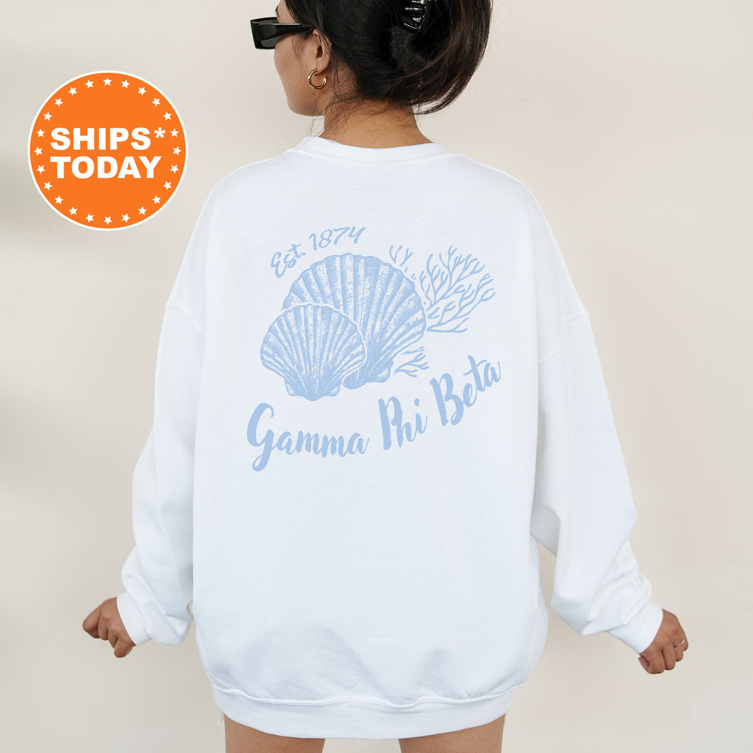 A woman wearing a white sweatshirt with a graphic design of seashells and the text "Gamma Phi Beta" printed on it.
