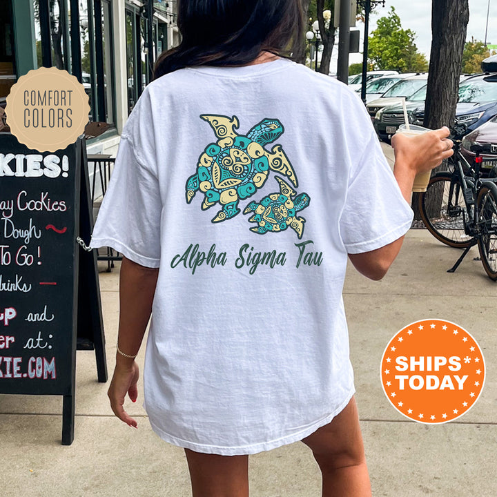 A person wearing a white t-shirt with a graphic of a turtle and the text "Alpha Sigma Tau" printed on it, standing on a sidewalk.