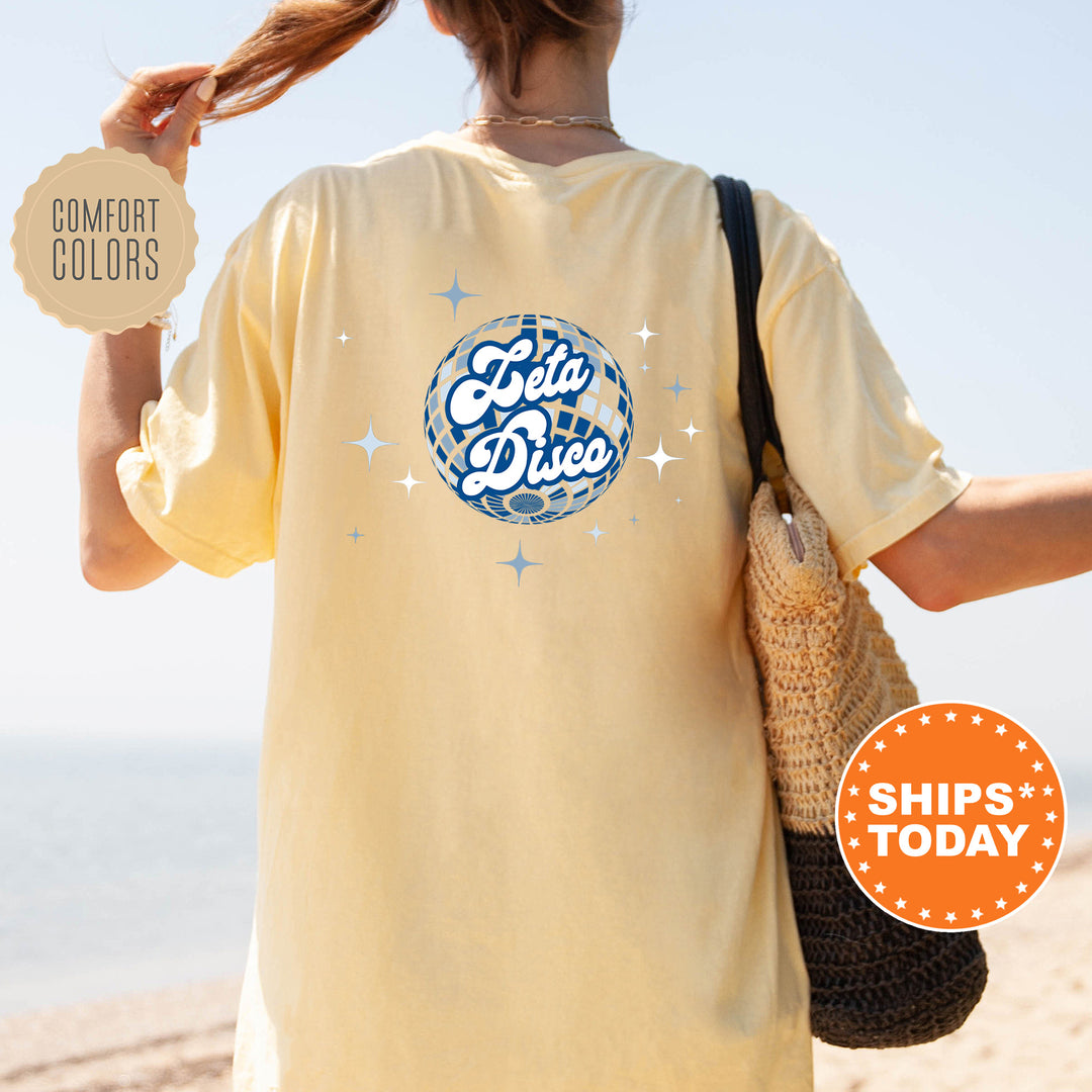A person wearing a yellow t-shirt with a graphic design and text, standing on a beach with a handbag.
