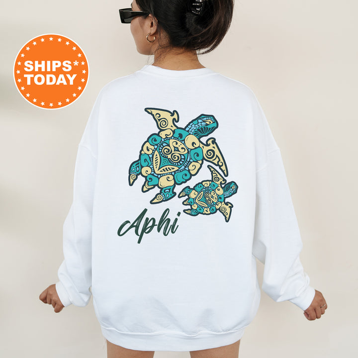 A woman wearing a white sweatshirt with a colorful turtle design and the word "APhi" printed on it.