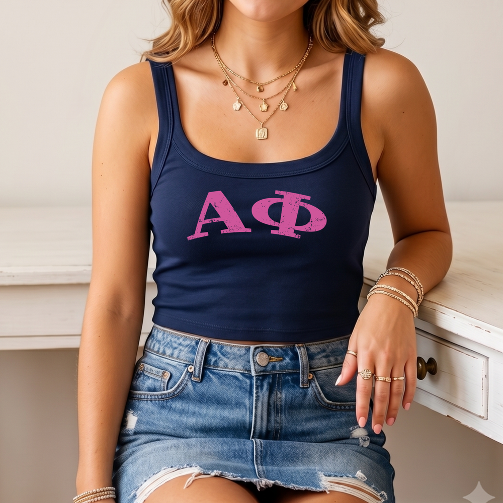 A woman wearing a navy blue crop top with the letters 'ΑΓΟ' printed on it, paired with a denim skirt and multiple rings on her fingers.