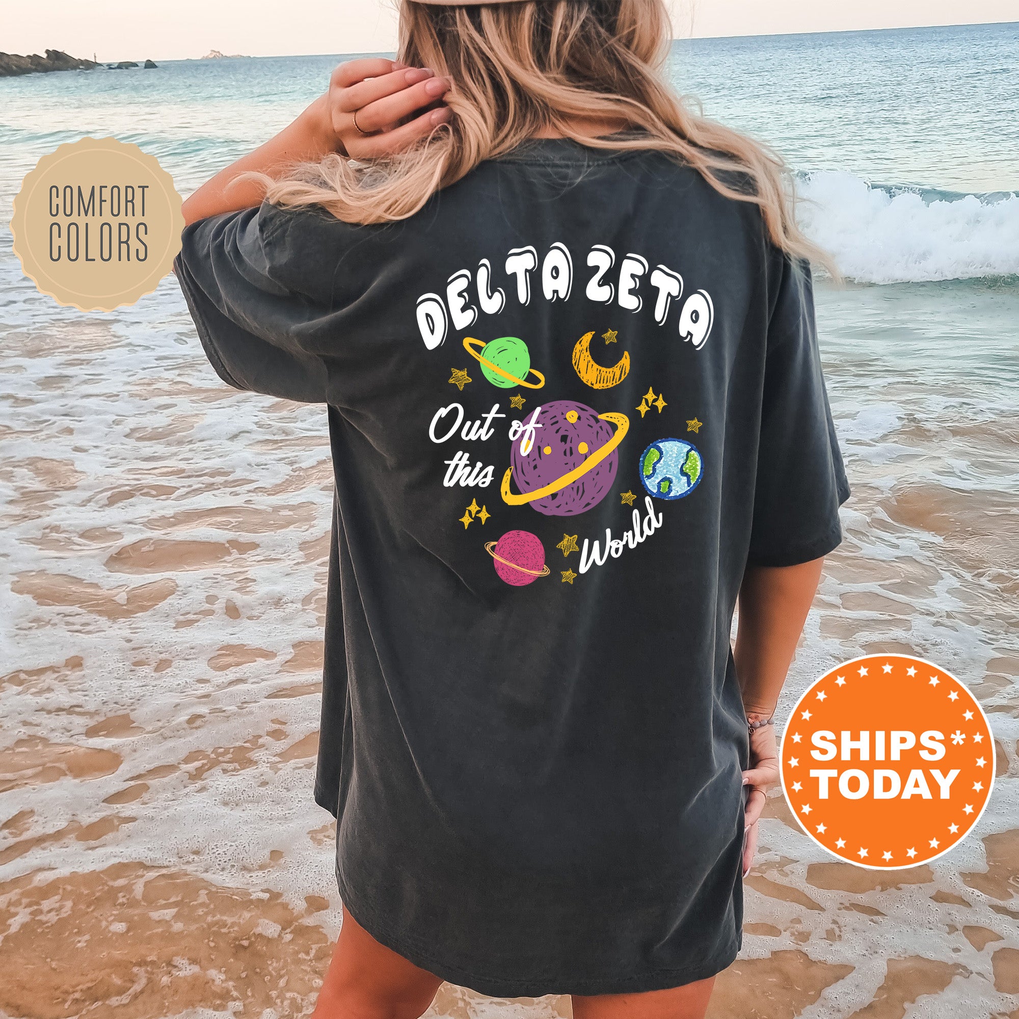 A woman wearing a black t-shirt with a colorful graphic design on the back, standing on a beach with the ocean in the background.
