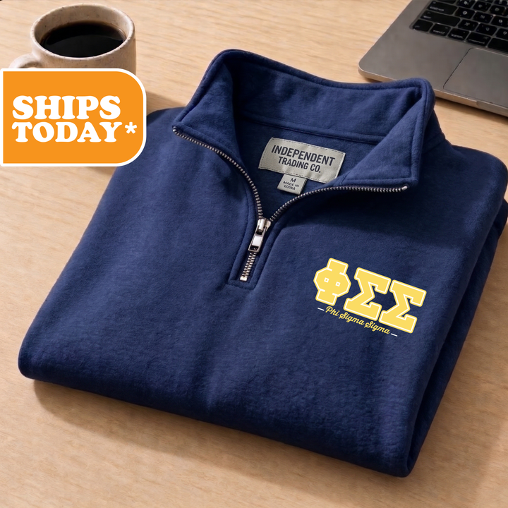 A navy blue zip-up jacket with a yellow Sigma Theta logo is displayed on a wooden surface, accompanied by a laptop and a coffee cup.