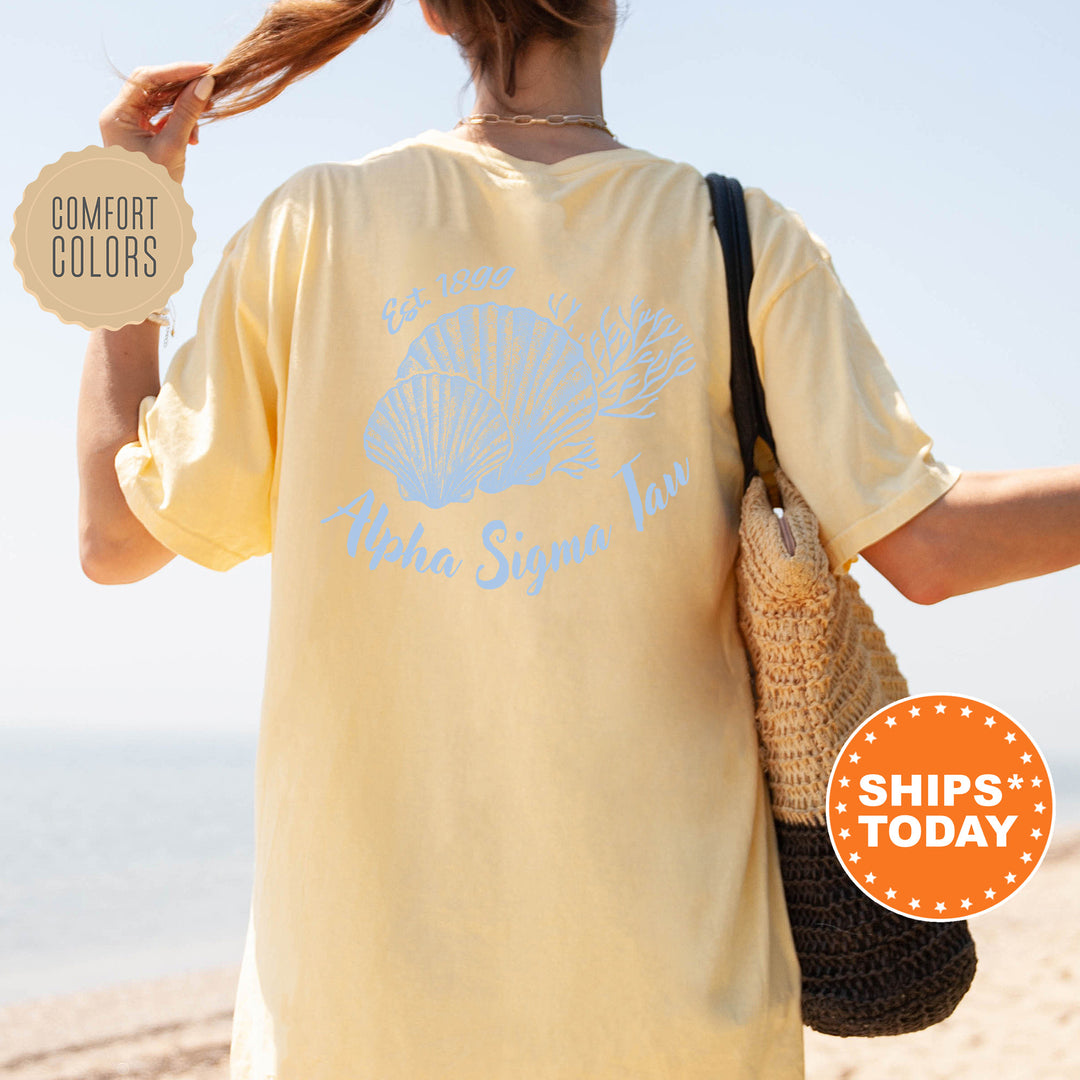 A person wearing a yellow t-shirt with a blue design and text, standing on a beach with a handbag and a sign advertising "SHIPS TODAY".