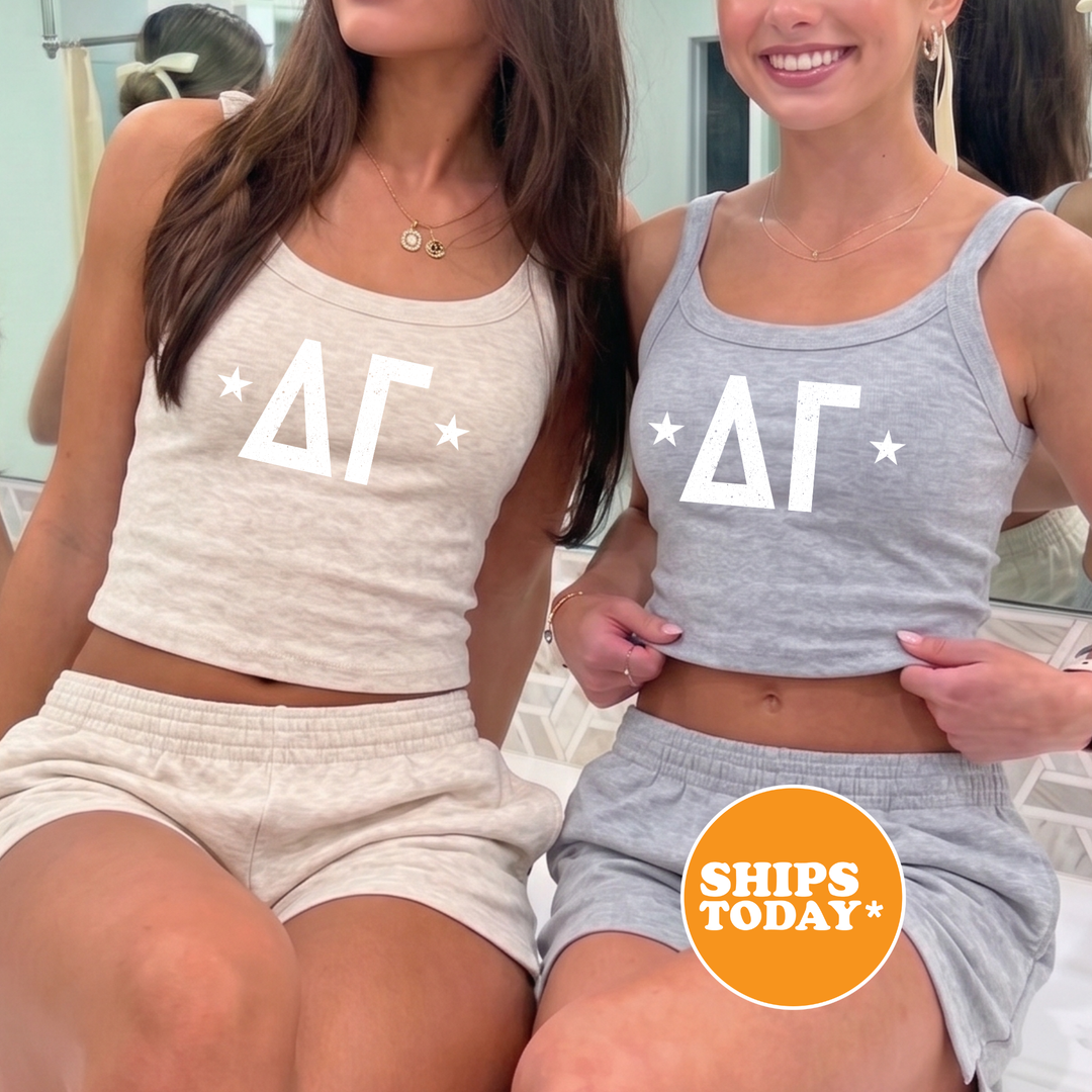 Two women wearing matching gray tank tops with white stars and the letters "ΑΓ" are sitting next to each other.