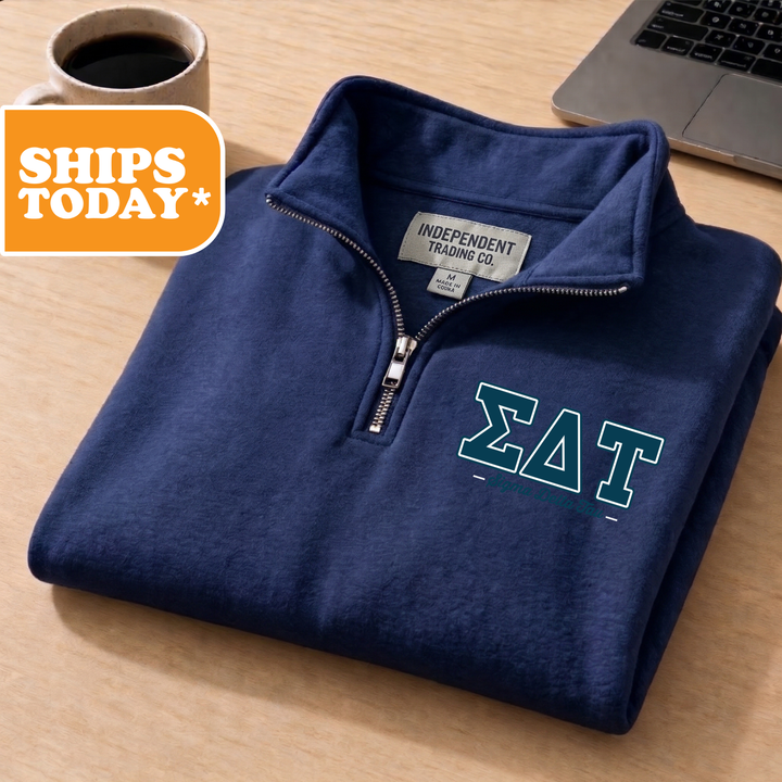 A navy blue zip-up jacket with the Greek letter 'ΑΛ' printed on the front, placed on a wooden surface next to a laptop.