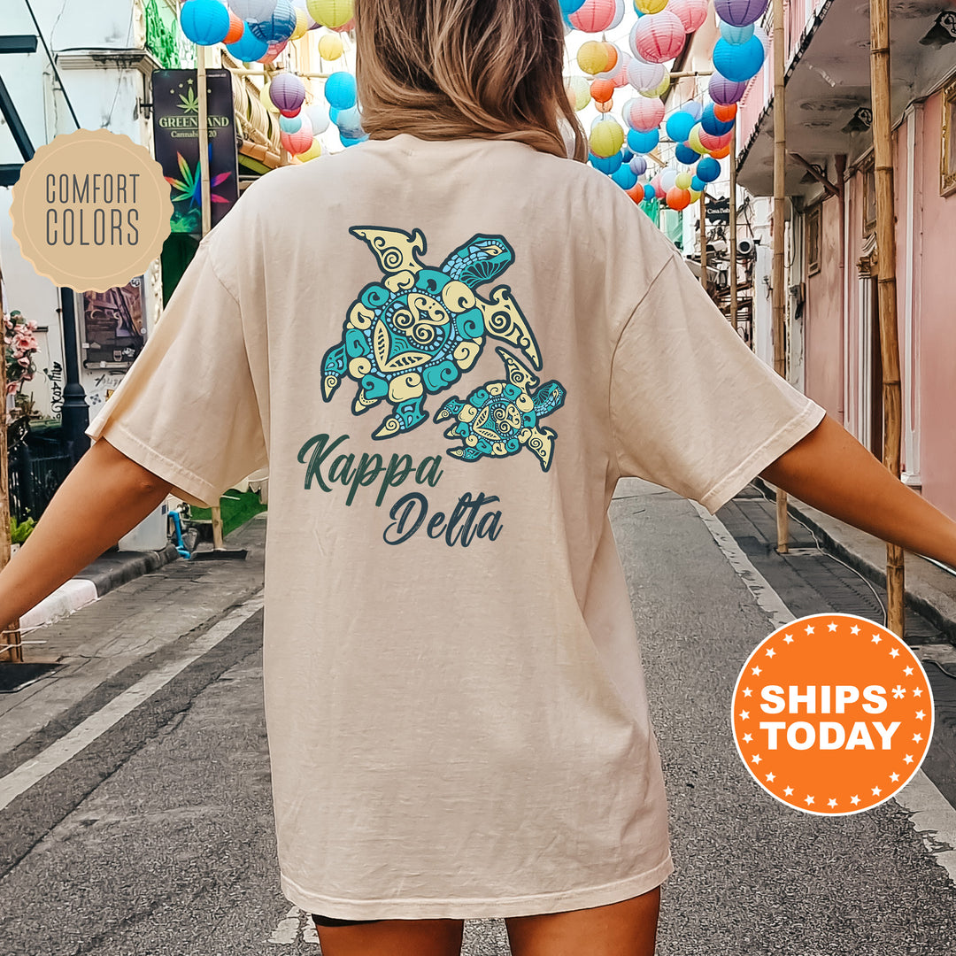A person wearing a beige t-shirt with a colorful turtle design and text printed on it, standing on a street with colorful lanterns hanging overhead.