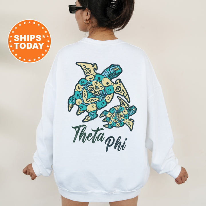 A woman wearing a white sweatshirt with a colorful graphic of a turtle and the text "Theta Phi" printed on the back.