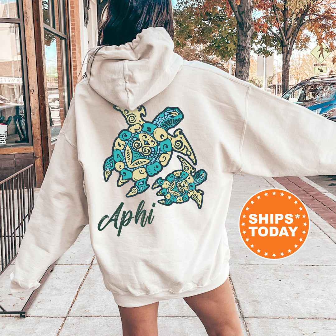 A person wearing a white hoodie with a colorful turtle design and the text "A phi" printed on it, standing on a sidewalk.