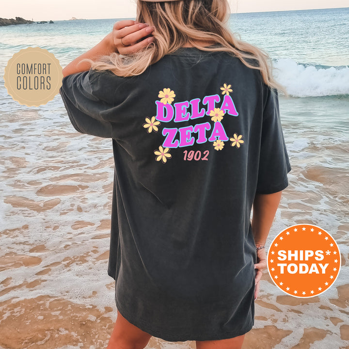 A woman wearing a black t-shirt with the text "DELTA ZETA" and "1902" printed on it, standing on a beach with waves in the background.