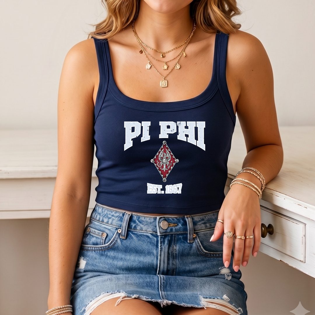 A woman wearing a navy blue crop top with white text and a red and white logo, paired with distressed denim shorts and multiple rings on her fingers.