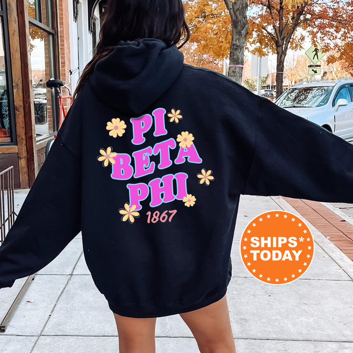 A person wearing a black hoodie with the text "PI BETA PHI" and "1867" printed on it, standing on a sidewalk with a car and a building in the background.