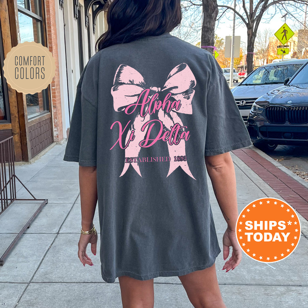 a woman walking down a sidewalk wearing a gray shirt with a pink bow on it