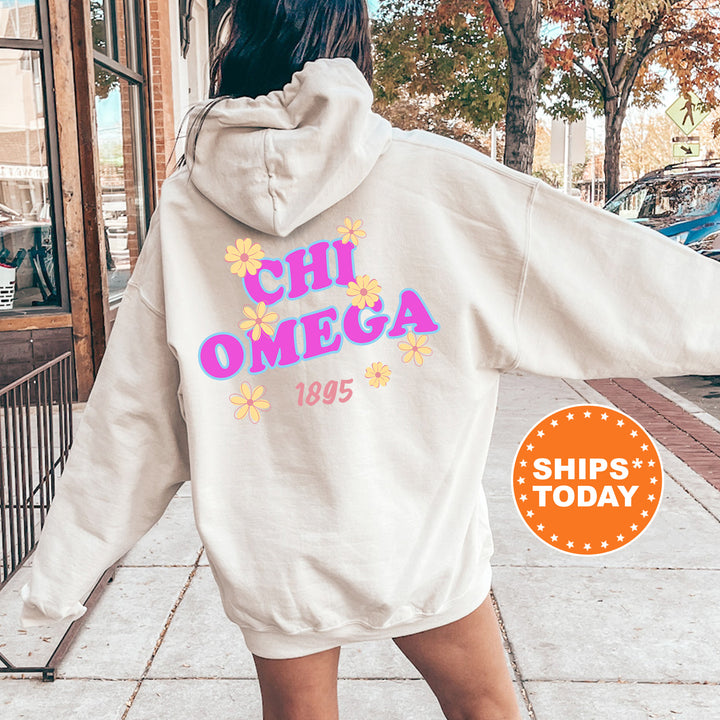 A person wearing a white hoodie with the text "CHI OMEGA" and "1895" printed on it, standing on a sidewalk with trees and a building in the background.