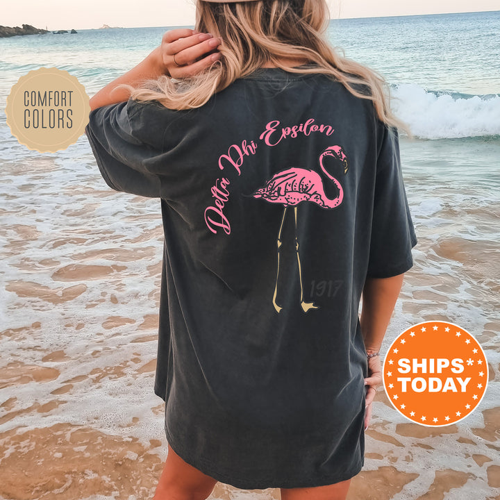 a woman standing on a beach wearing a black shirt with a pink flamingo on