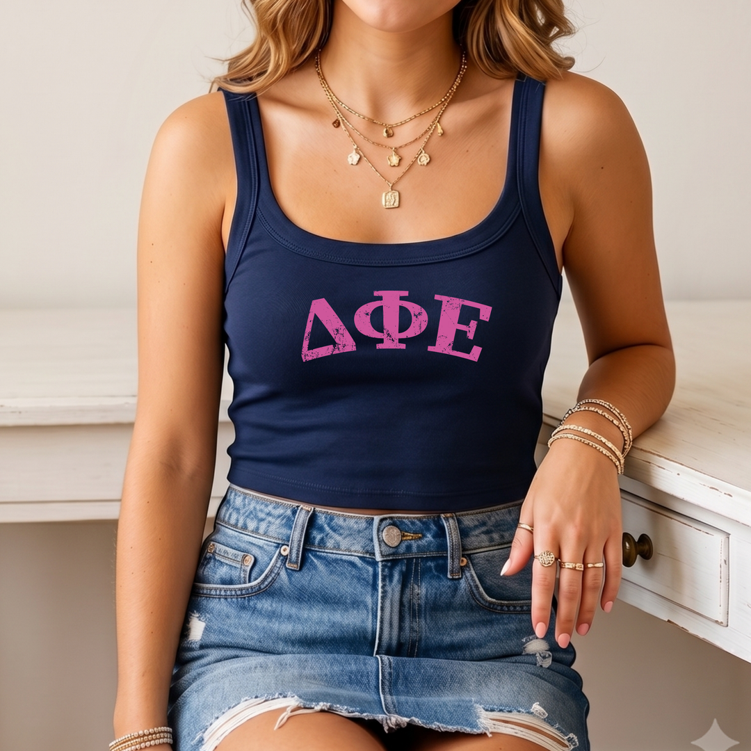 A woman wearing a navy blue crop top with the letters "ΦΕΛΙ" printed on it, paired with a denim skirt and multiple rings on her fingers.
