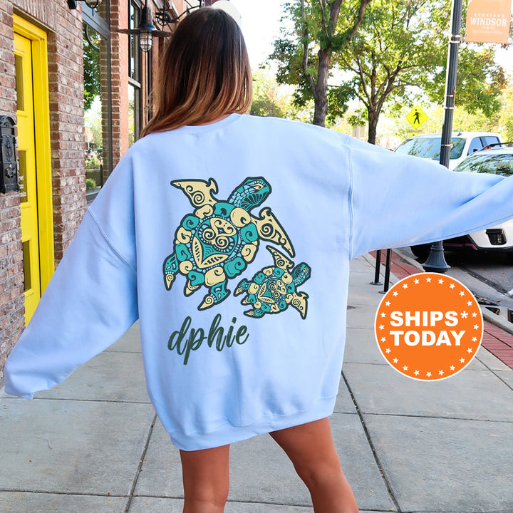 A woman wearing a light blue sweatshirt with a colorful turtle design on the back, standing on a sidewalk.