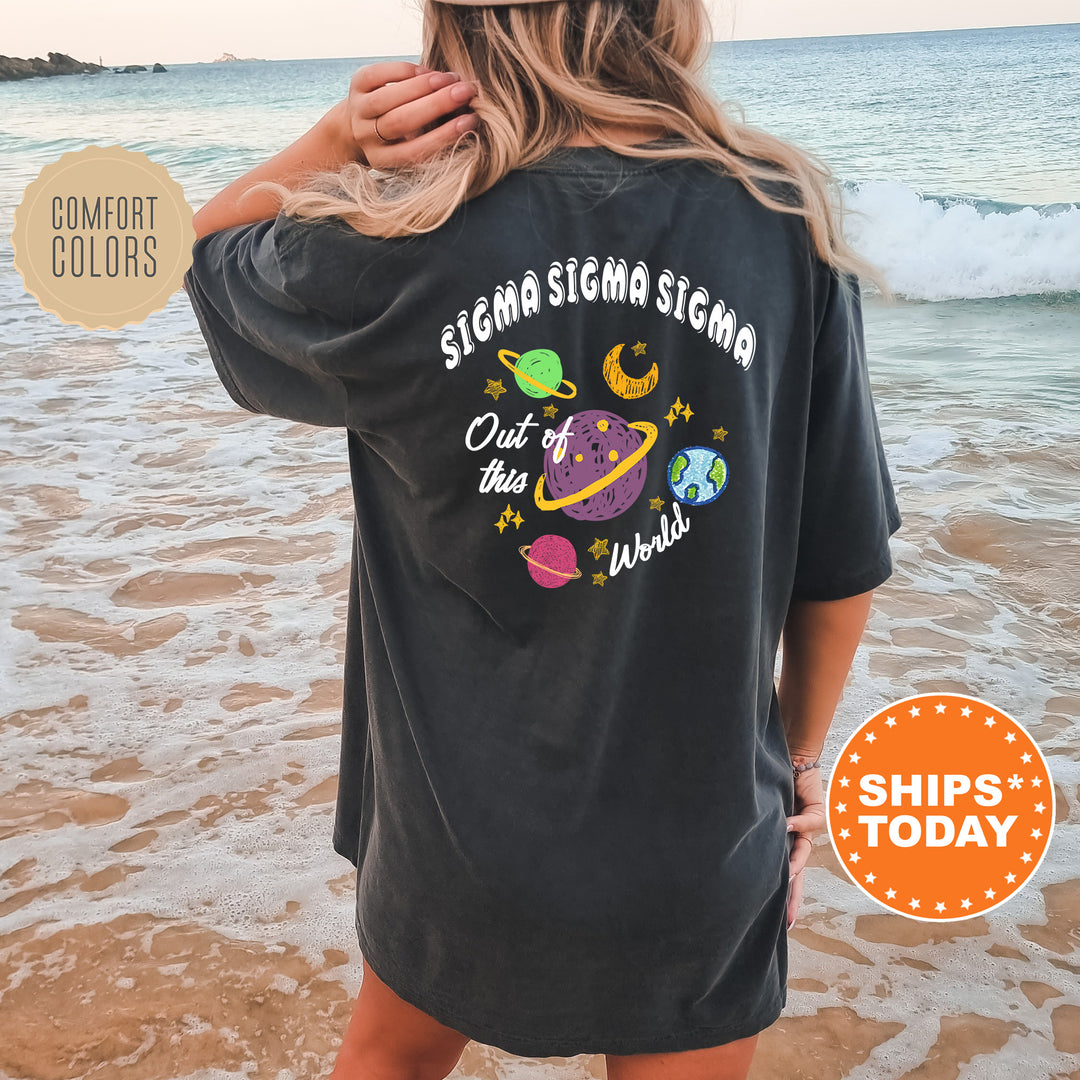 A woman wearing a black t-shirt with a graphic design of planets and stars on the back, standing on a beach with the ocean in the background.