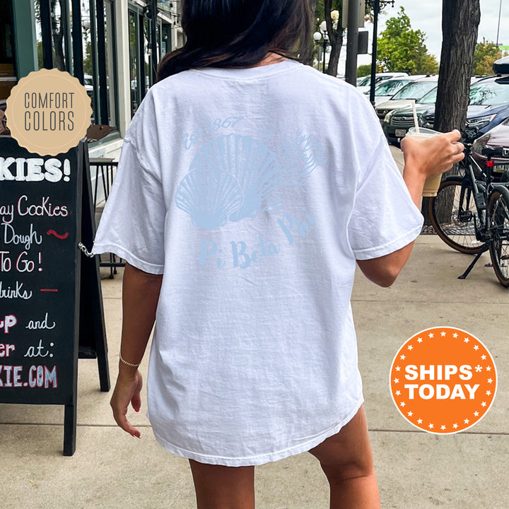A person wearing a white t-shirt with a graphic design on the back is walking on a sidewalk, with a chalkboard sign and bicycles visible in the background.