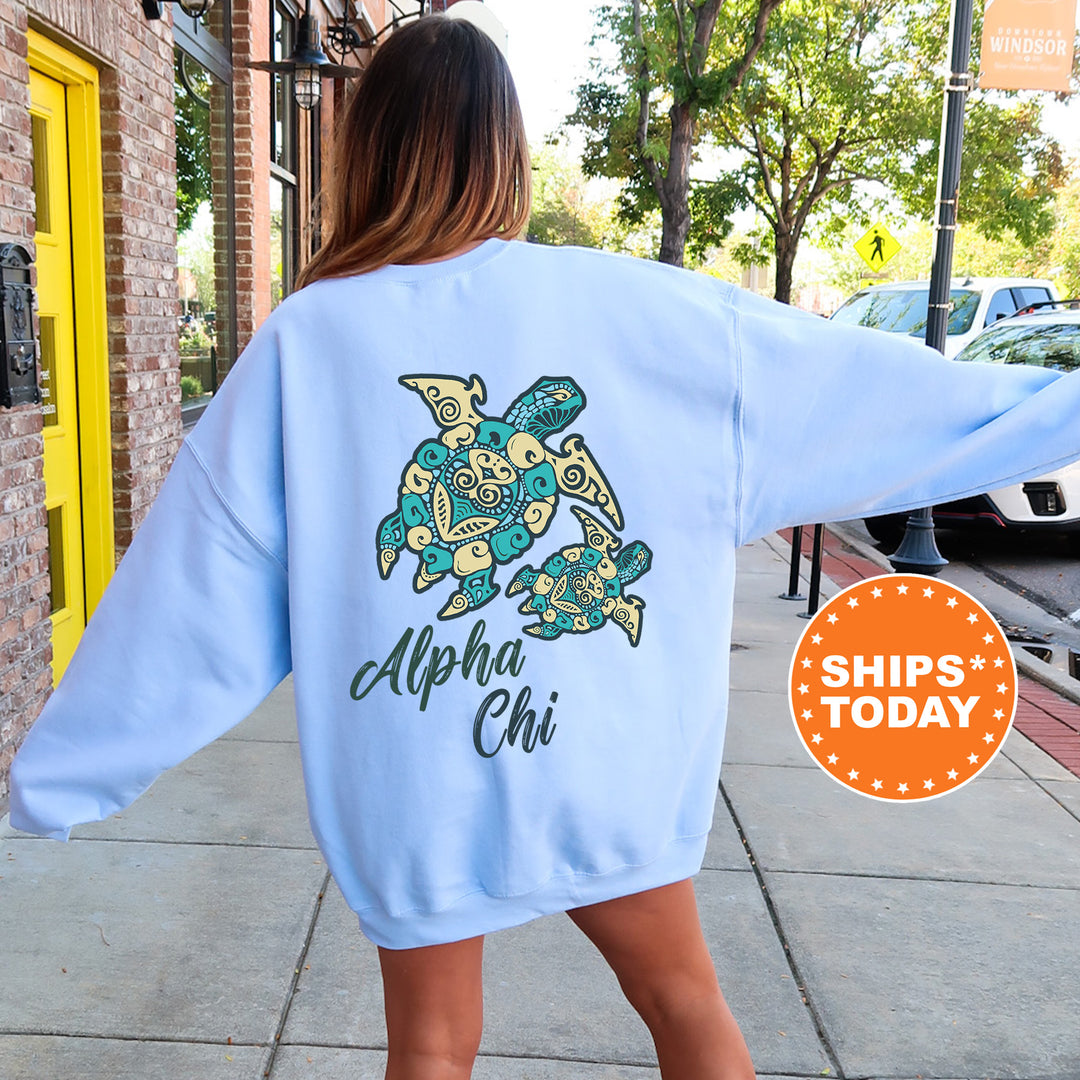 A woman wearing a light blue sweatshirt with a graphic of a turtle and the text "Alpha Chi" printed on it, standing on a sidewalk.
