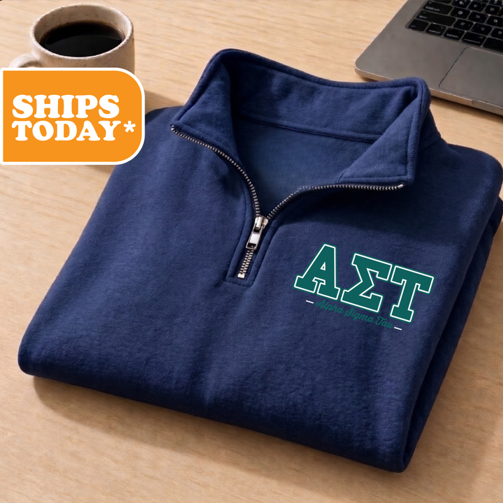 A navy blue zip-up jacket with the letters 'ΣΛΑ' printed on it, placed on a wooden surface next to a laptop.