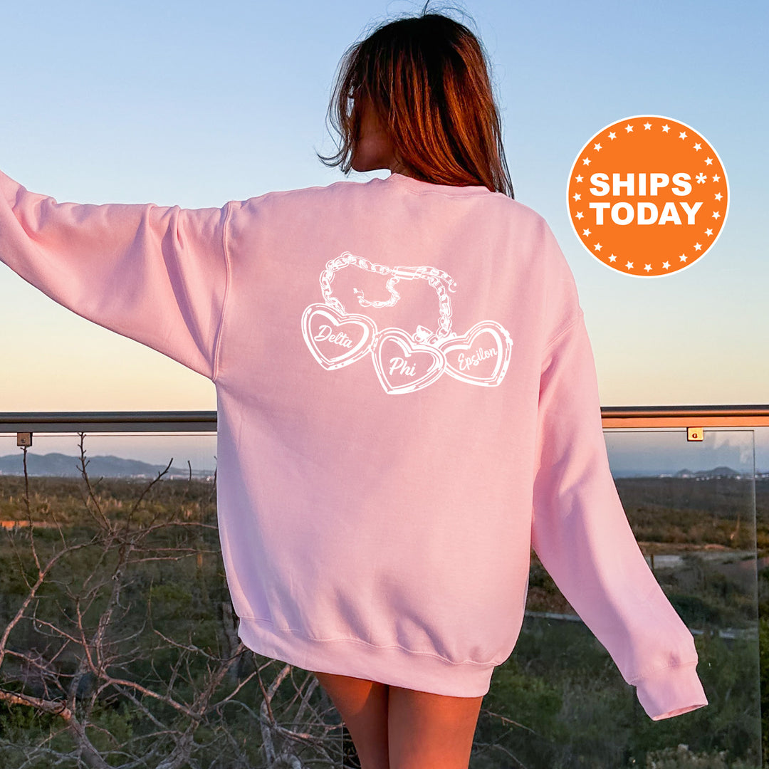A woman wearing a pink sweatshirt with a graphic design on the back, standing in front of a scenic outdoor landscape with mountains in the distance.