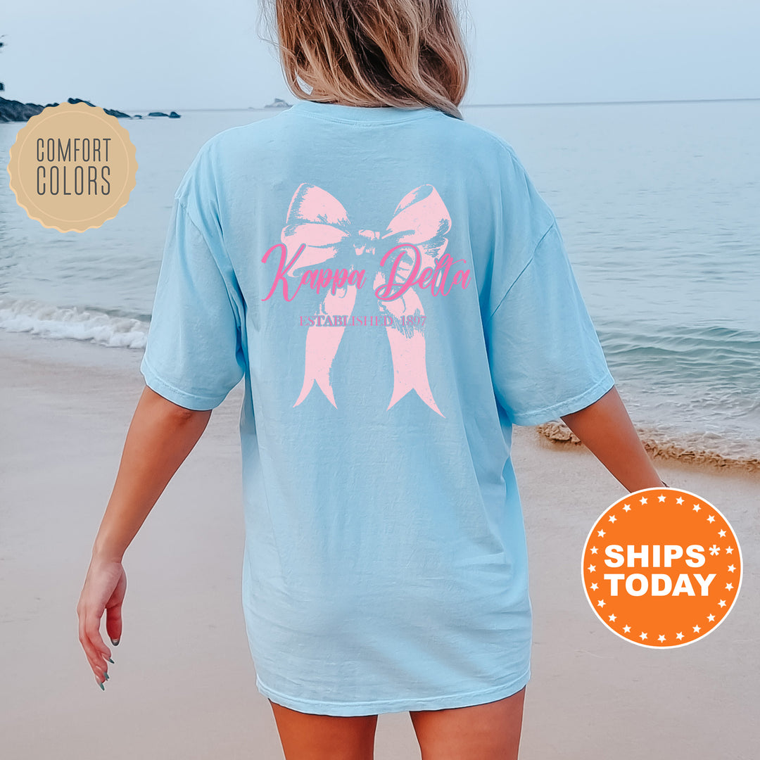 a woman walking on the beach wearing a blue shirt with a pink bow on it