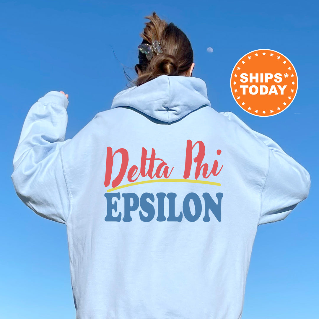 A person wearing a white hoodie with the Delta Phi Epsilon logo printed on it, standing against a clear blue sky.
