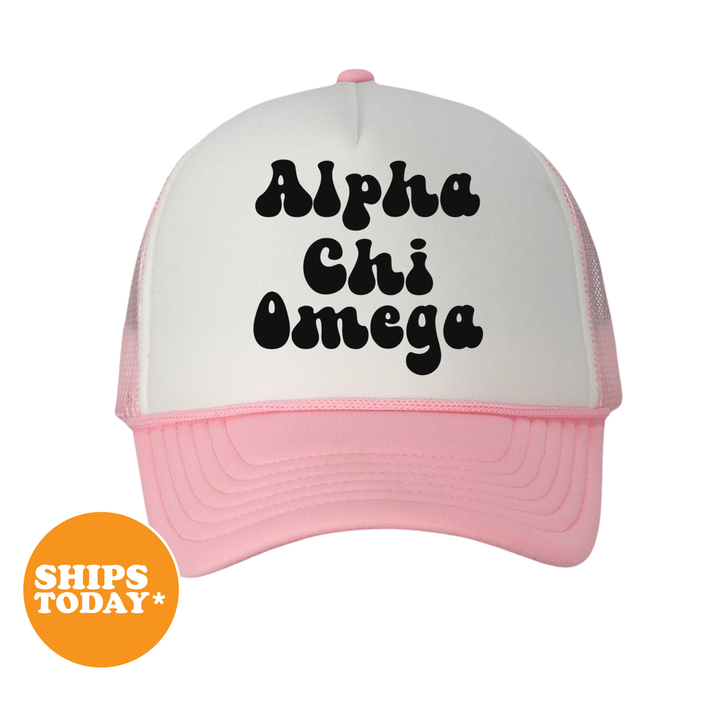 A pink and white baseball cap with the text "Alpha Chi Omega" printed on it.