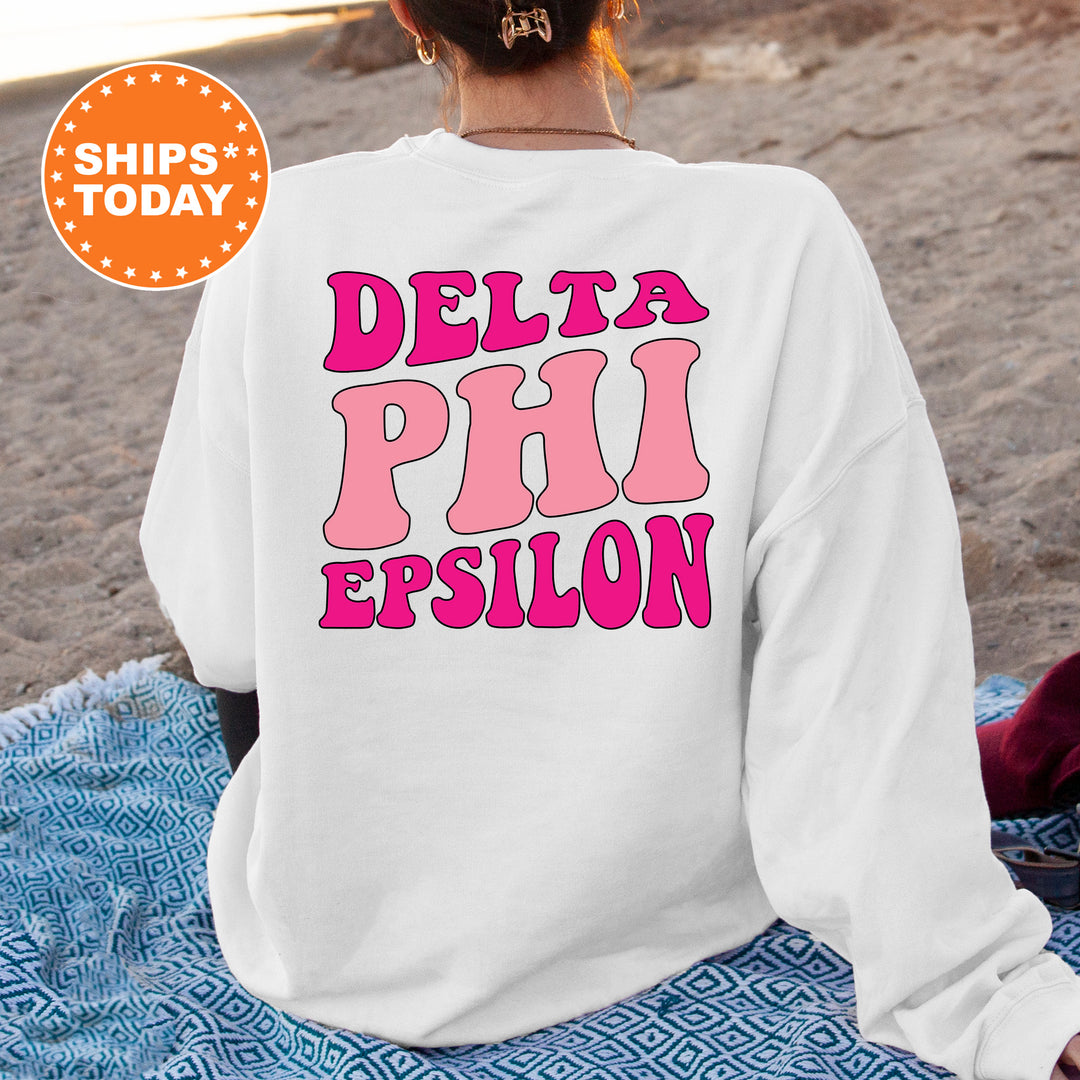 a woman sitting on the beach wearing a sweatshirt that says delta phi epiloon