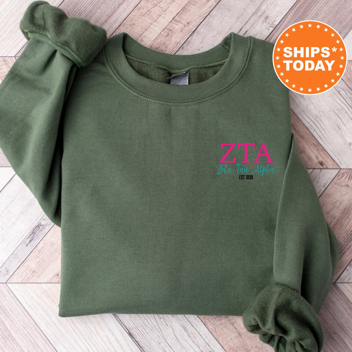 a green sweatshirt with a pink zta logo on it