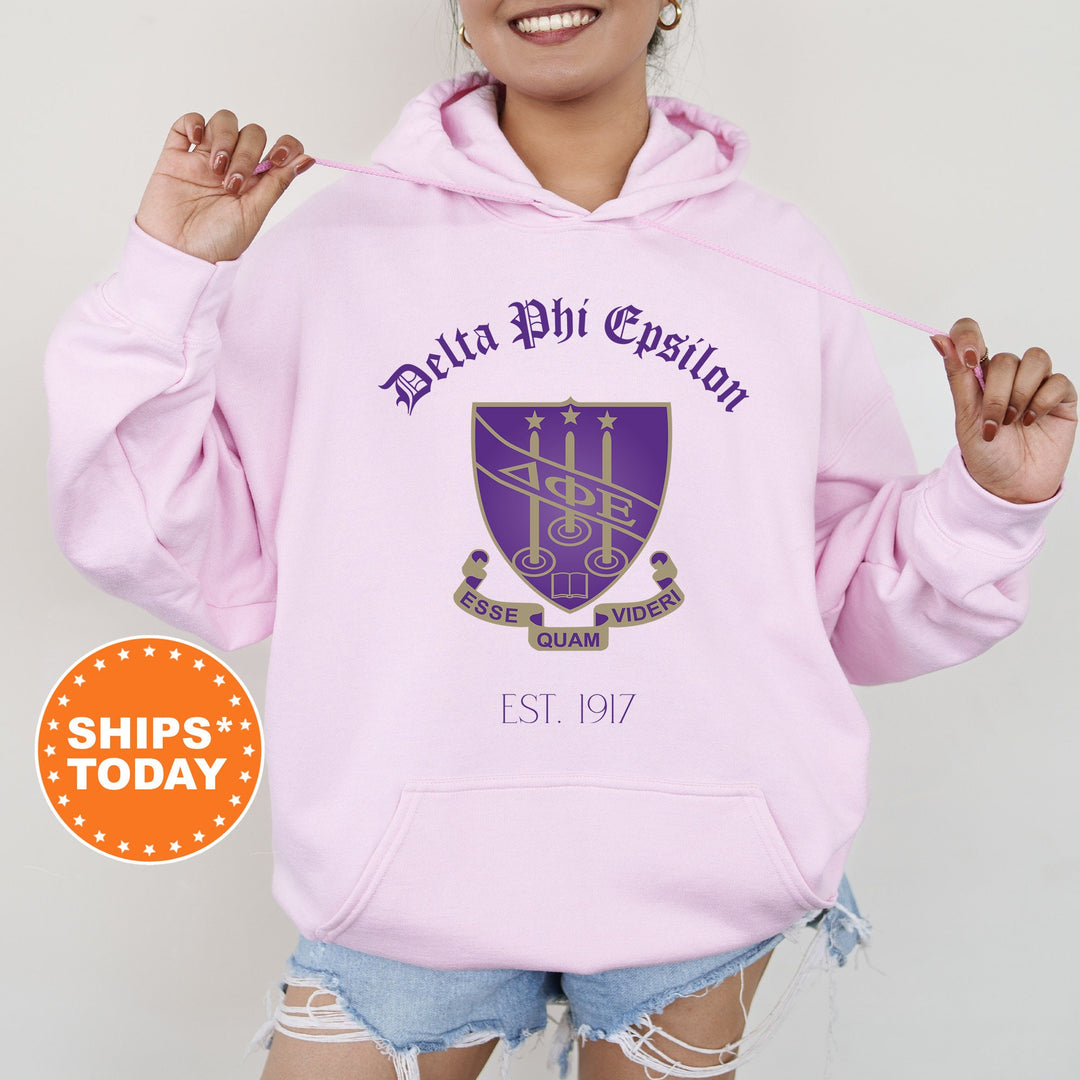 a woman wearing a pink hoodie with a purple crest on it