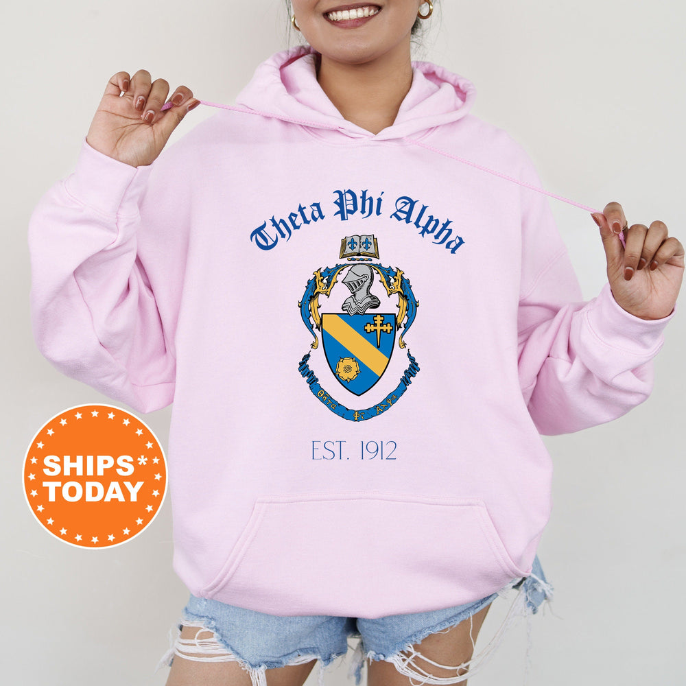 a woman wearing a pink hoodie with a coat of arms on it