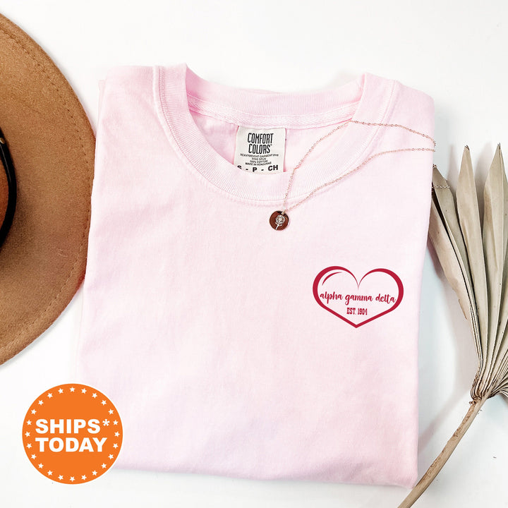 a pink shirt with a heart on it next to a hat
